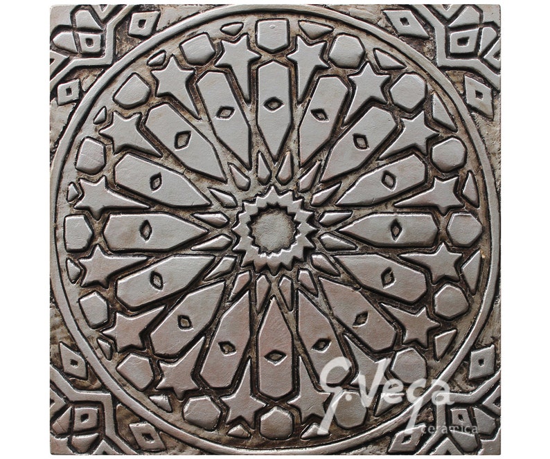 May include: A silver ceramic tile with an intricate geometric design featuring a central starburst surrounded by smaller stars and geometric shapes.