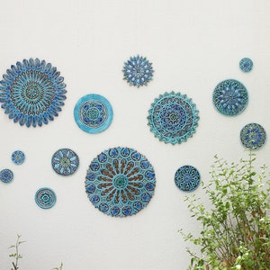 May include: A white wall with a collection of blue and green ceramic wall decor in various sizes and patterns. The decor features intricate designs with floral and geometric motifs.