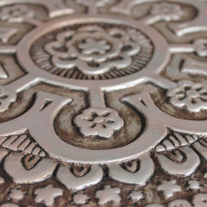 May include: Close-up of a silver and brown decorative tile with an intricate floral pattern.