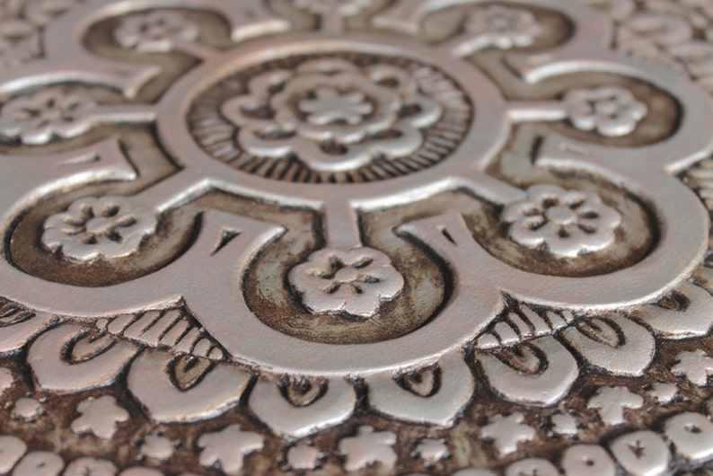 May include: Close-up of a silver and brown decorative tile with an intricate floral pattern.