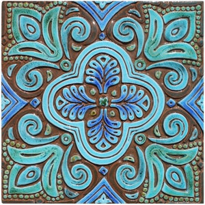 Può includere: Una piastrella quadrata in ceramica con un motivo geometrico blu e verde. La piastrella ha uno sfondo marrone e presenta intricati vortici e disegni floreali.