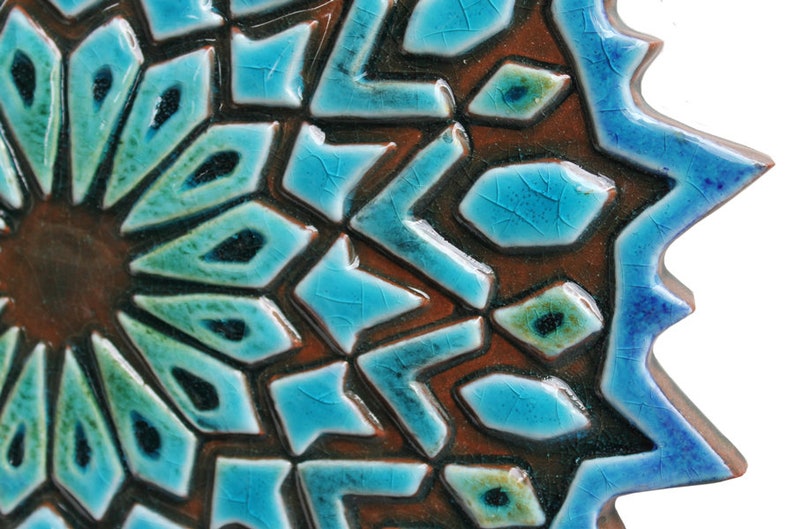 May include: A close-up of a blue and brown ceramic tile with a geometric pattern. The tile has a starburst design with a raised center and a textured surface.
