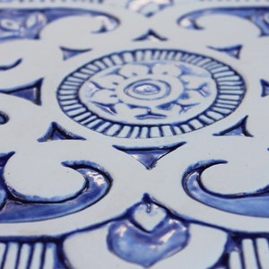 May include: A close-up of a white ceramic tile with a blue and white floral design. The tile has a raised, embossed pattern.