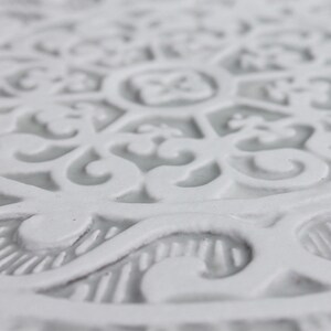 May include: White ceramic coaster with an intricate, embossed, floral design.