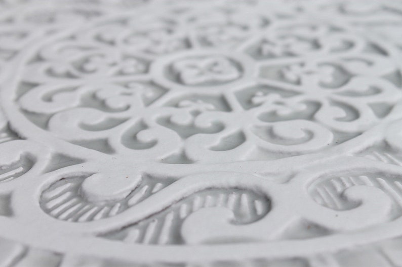 May include: White ceramic coaster with an intricate, embossed, floral design.