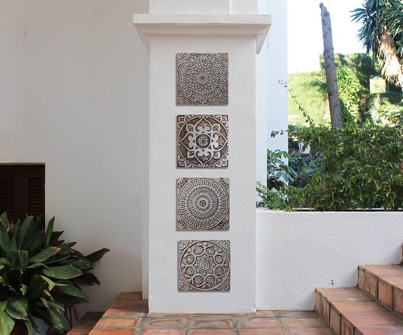 May include: Four square wall decor pieces with intricate, embossed, mandala-like designs in shades of brown and white. The pieces are arranged vertically on a white wall.