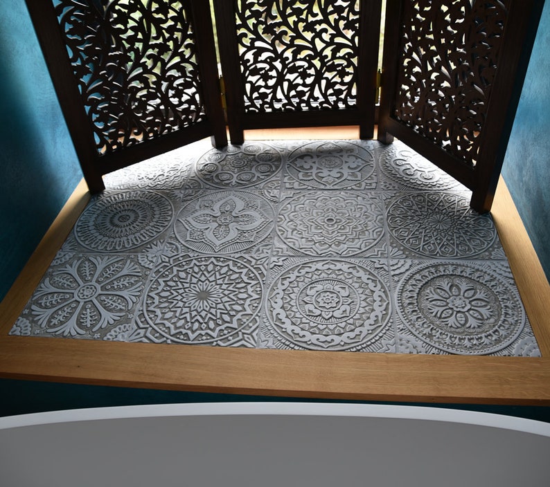 May include: A close-up of a bathroom floor with gray patterned tiles. The tiles have a raised, embossed design. The floor is bordered by a wooden trim.
