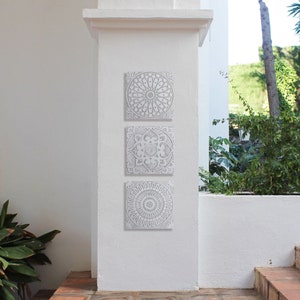 May include: Three white ceramic wall tiles with intricate geometric designs. The tiles are arranged vertically on a white wall.