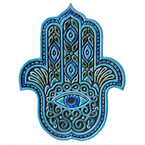 Op de afbeelding: Een blauwe en groene keramische Hamsa-hand met een boze oog in het midden. De Hamsa-hand is een symbool van bescherming en geluk.