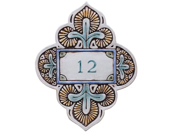 May include: A ceramic house number plaque with a decorative design in shades of blue, green, and yellow. The number "12" is displayed in a white rectangle.