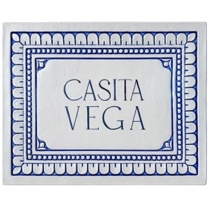 Op de afbeelding: Witte keramische tegel met een blauwe rand en de tekst "CASITA VEGA" in blauwe letters.
