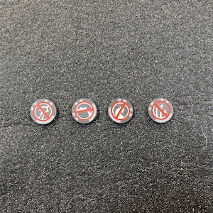 May include: Four small, round tokens with a gray border and a red prohibition symbol in the center. The symbols vary, depicting different actions or objects. The tokens are on a textured, dark gray surface.