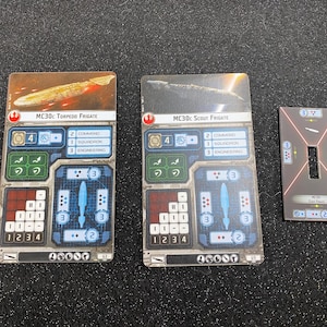 May include: Three Star Wars Armada game cards. Two rectangular cards feature ship illustrations and text, including "MC30c Torpedo Frigate" and "MC30c Scout Frigate." A smaller, rectangular card has a central cutout and red lines.