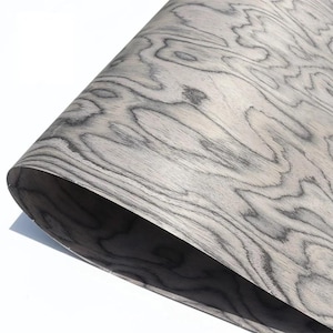 May include: A sheet of wood veneer with a swirling, organic grain pattern in shades of grey and white. The wood appears flexible and slightly curled, revealing a darker underside. The overall effect is a natural, textured surface.