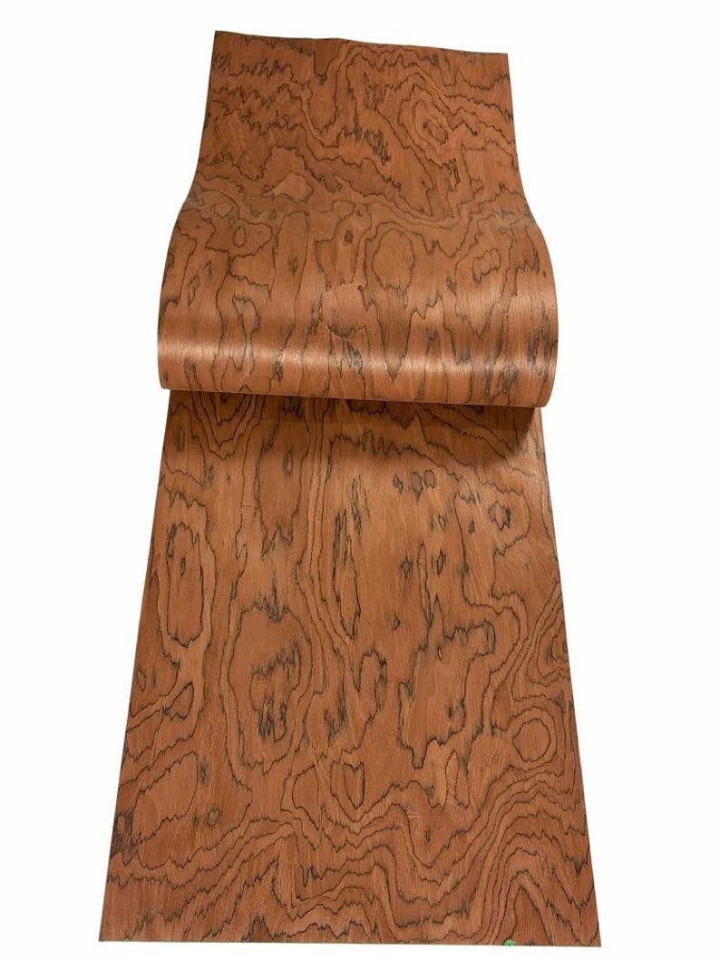 K&ouml;nnte beinhalten: Ein Holzfurnierblatt in einem satten, rotbraunen Farbton mit einem ausgepr&auml;gten, wirbelnden Maserungsmuster. Das Furnier ist teilweise gerollt und zeigt die komplizierten Details des nat&uuml;rlichen Designs des Holzes. Das Holz scheint glatt und bereit f&uuml;r Holzbearbeitungsprojekte zu sein.