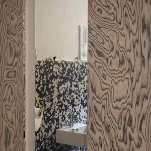 Puede incluir: Vista interior de un ba&ntilde;o con dise&ntilde;o moderno. Las paredes presentan un patr&oacute;n de vetas de madera &uacute;nico en tonos grises y beige. Se ven un lavabo blanco y una pared estampada con manchas blancas y negras.