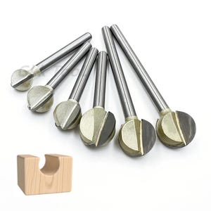 Puede incluir: Un juego de seis fresas de bola plateadas y grises con vástagos cilíndricos. En primer plano, un pequeño bloque de madera de color claro con un recorte curvo. Las fresas están diseñadas para trabajar la madera.