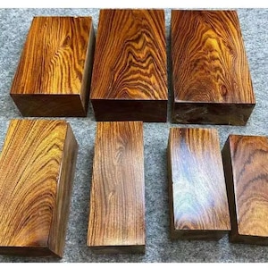 Puede incluir: Siete bloques rectangulares de madera con un color marrón cálido y rico y patrones de vetas intrincados. La madera tiene un aspecto pulido, mostrando la belleza natural del material. Los bloques varían en tamaño y forma, para proyectos de carpintería.