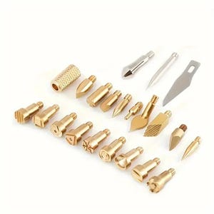 Puede incluir: Un conjunto de herramientas para pirograbado con diversas puntas y cuchillas. El juego incluye puntas de latón de diferentes formas, incluyendo diseños puntiagudos, angulados y estampados, junto con cuchillas plateadas. Las herramientas están dispuestas sobre una superficie blanca.