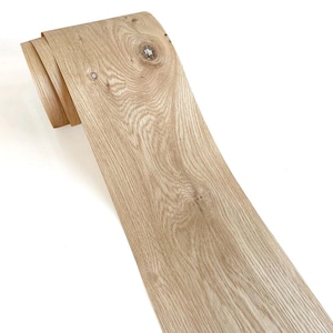 Könnte beinhalten: Eine Rolle hellbraunes Holzfurnier mit sichtbarer Maserung und einem Astloch. Das Furnier ist oben gerollt, wodurch die Schichten sichtbar werden. Das Holz hat ein natürliches, unfertiges Aussehen.