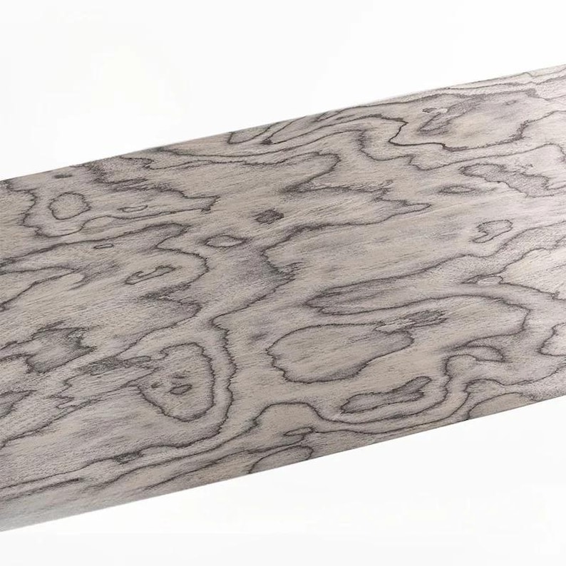 K&ouml;nnte beinhalten: Nahaufnahme eines Holzabschnitts mit einem einzigartigen Maserungsmuster. Das Holz hat eine hellgraue Grundfarbe mit dunkelgrauen, wirbelnden Mustern. Die Maserung erzeugt ein organisches, flie&szlig;endes Design, ideal f&uuml;r Holzbearbeitungsprojekte.