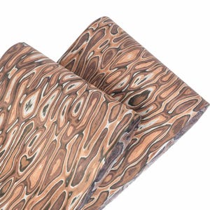 Puede incluir: Dos rollos de tela con un patr&oacute;n de vetas de madera. La tela presenta una mezcla de colores marr&oacute;n, beige y blanco, creando un dise&ntilde;o naturalista. El material parece suave y flexible, adecuado para diversos proyectos de artesan&iacute;a.
