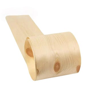 Może przedstawiać: Zwinięty arkusz jasnego forniru drewnianego z widocznymi słojami i sękami. Drewno ma naturalny, jasny odcień, a wzór słojów tworzy teksturowany wygląd. Fornir jest zwinięty, co sugeruje elastyczność i przydatność do różnych projektów stolarskich.