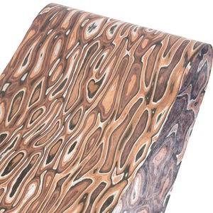 Puede incluir: Un rollo de papel con un dise&ntilde;o de vetas de madera. El dise&ntilde;o presenta l&iacute;neas onduladas en tonos marr&oacute;n, beige y blanco, creando un aspecto natural y org&aacute;nico. El papel est&aacute; enrollado, mostrando el patr&oacute;n en la superficie.