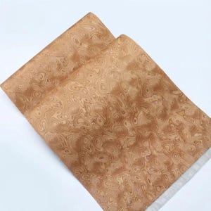 May include: Two sheets of light brown paper with a wood grain pattern. The paper has a swirling, organic design in shades of tan and brown. The paper is layered on a white background.