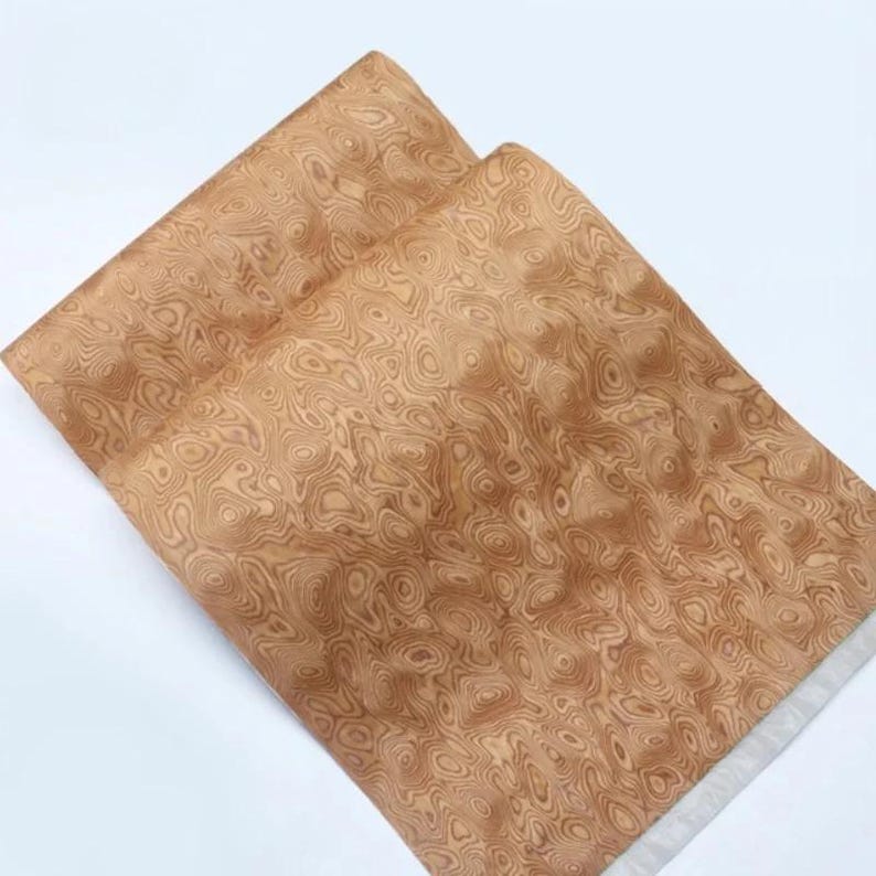 May include: Two sheets of light brown paper with a wood grain pattern. The paper has a swirling, organic design in shades of tan and brown. The paper is layered on a white background.