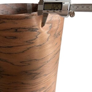 K&ouml;nnte beinhalten: Nahaufnahme eines digitalen Messschiebers, der die Dicke eines Materials mit Holzmaserung misst. Der Messschieber zeigt ein Ma&szlig; von 0,64 cm an. Das Material hat eine braune und schwarze Farbgebung.
