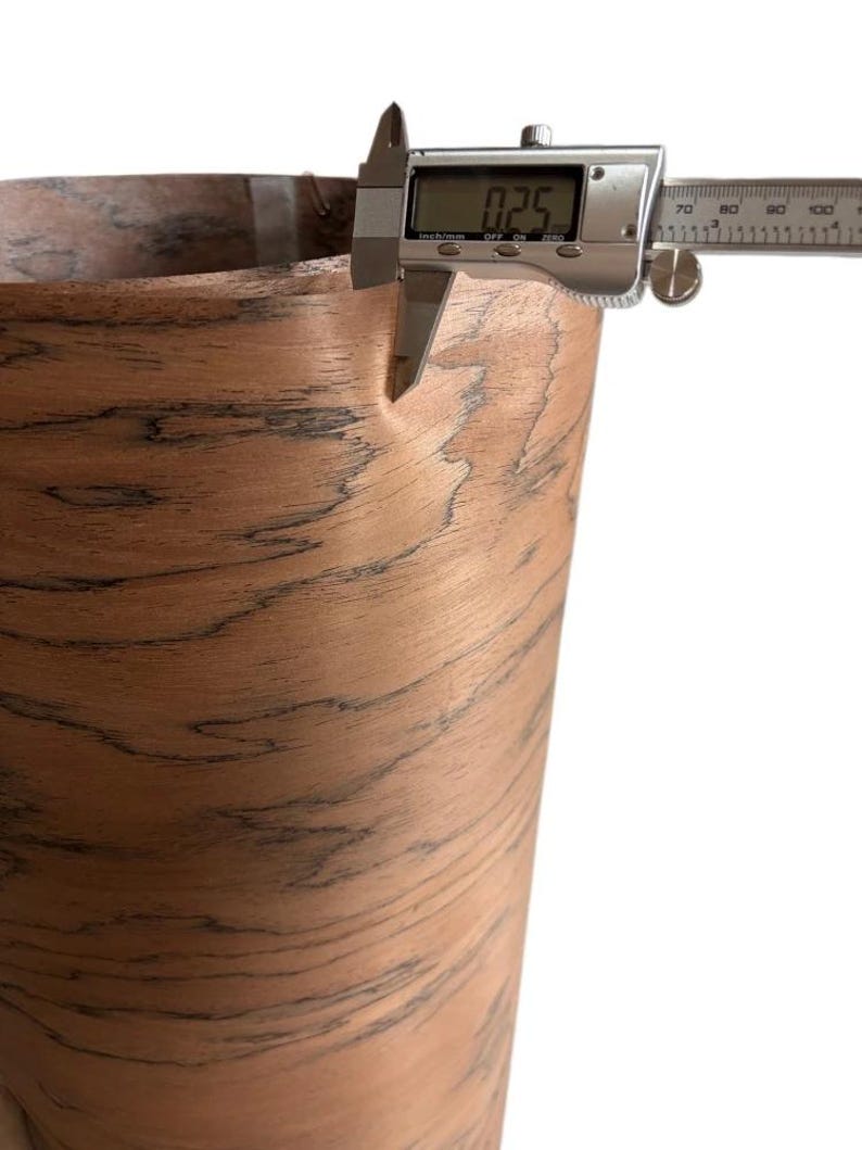K&ouml;nnte beinhalten: Nahaufnahme eines digitalen Messschiebers, der die Dicke eines Materials mit Holzmaserung misst. Der Messschieber zeigt ein Ma&szlig; von 0,64 cm an. Das Material hat eine braune und schwarze Farbgebung.