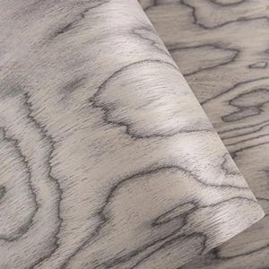 K&ouml;nnte beinhalten: Nahaufnahme eines hellgrauen Holzmaserungsmusters mit dunkelgrauen Wirbelmustern. Das Holz scheint ein Blatt oder eine Rolle zu sein, wobei ein Teil davon umgefaltet ist, wodurch die Textur und die Farbvariationen sichtbar werden.