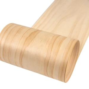 Może przedstawiać: Zwinięty arkusz jasnego forniru drewnianego. Widoczne usłojenie drewna, z odcieniami od jasnobeżowego do nieco ciemniejszego brązu. Fornir jest elastyczny i wydaje się być świeżo wyprodukowany.