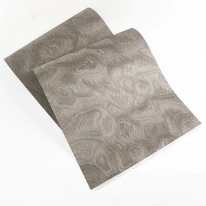 May include: Two sheets of gray decorative paper with a swirling wood grain pattern. The paper has a light gray base color with darker gray and white swirling patterns. The sheets are slightly overlapping, with the edges visible.