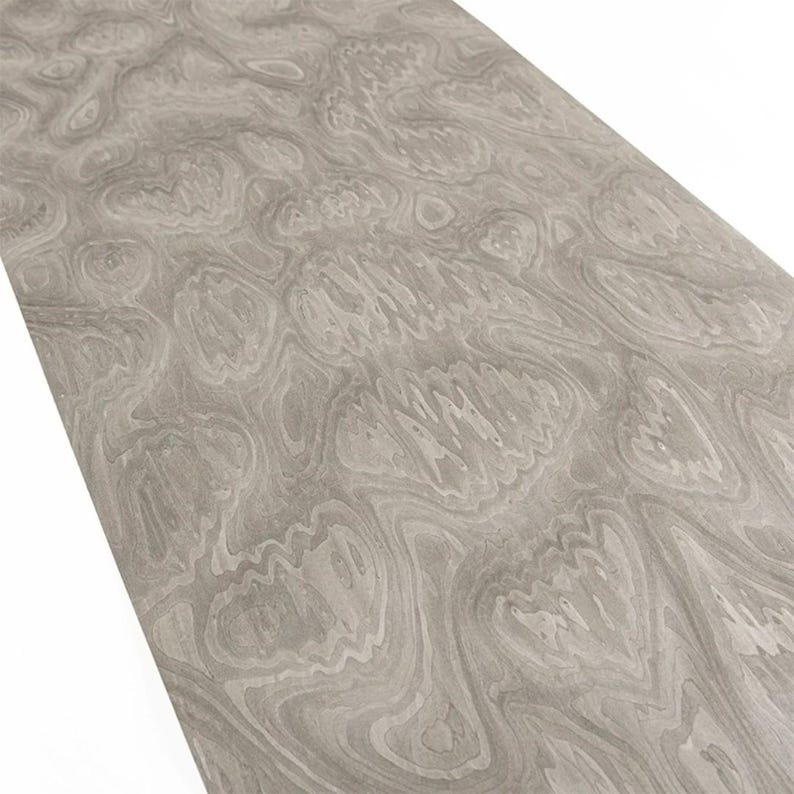 May include: A close-up of a piece of wood with a swirling, organic pattern. The wood grain features shades of gray and white, creating a marbled effect. The surface is angled, revealing the texture and detail of the wood.