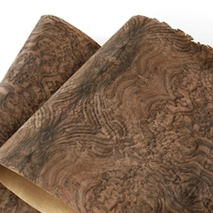 May include: Two sheets of wood veneer with a distinctive swirling grain pattern. The veneer displays a mix of brown and dark grey tones, with the edges slightly curled. The sheets reveal a lighter backing material.