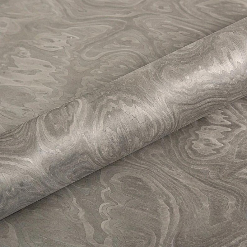 May include: A roll of gray marbled paper with a swirling pattern. The paper has a smooth, glossy finish and a subtle variation in tone, creating a sense of depth and texture. The design resembles natural stone.