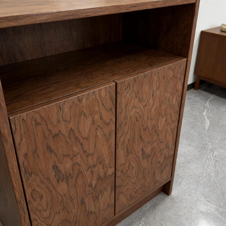 K&ouml;nnte beinhalten: Ein dunkelbrauner Holzschrank mit zwei T&uuml;ren und einem offenen Regal. Der Schrank hat ein nat&uuml;rliches Holzmaserungsmuster und ein schlichtes, modernes Design. Die T&uuml;ren sind geschlossen und der Schrank scheint neu zu sein.