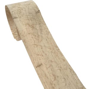 Peut inclure: Un rouleau de placage de bois de couleur claire avec un motif de grain naturel. Le placage est de couleur beige clair avec des stries et des tourbillons bruns plus foncés. Deux agrafes fixent l'extrémité enroulée. Le placage est pour la menuiserie.