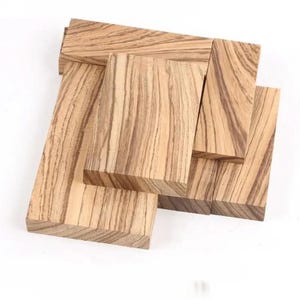 May include: A collection of rectangular wooden blocks with a distinctive zebrawood grain pattern. The blocks vary in size and are arranged in a layered composition, showcasing the natural wood tones and grain details.