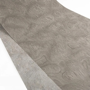 May include: A sheet of gray wood veneer with a swirling, organic grain pattern. The veneer has a light, neutral color and a smooth surface. The wood grain creates a natural, flowing design, suitable for furniture or decorative projects.