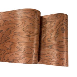 K&ouml;nnte beinhalten: Zwei Holzfurnierbl&auml;tter in einem r&ouml;tlich-braunen Farbton mit einem markanten Maserungsmuster. Die Holzmaserung weist dunkle, wellenf&ouml;rmige Linien auf, die eine einzigartige Textur erzeugen. Die Bl&auml;tter sind gerollt und zeigen die Flexibilit&auml;t und Form des Materials.
