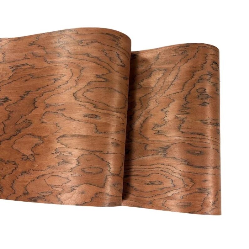 K&ouml;nnte beinhalten: Zwei Holzfurnierbl&auml;tter in einem r&ouml;tlich-braunen Farbton mit einem markanten Maserungsmuster. Die Holzmaserung weist dunkle, wellenf&ouml;rmige Linien auf, die eine einzigartige Textur erzeugen. Die Bl&auml;tter sind gerollt und zeigen die Flexibilit&auml;t und Form des Materials.