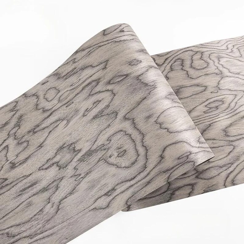 K&ouml;nnte beinhalten: Zwei Holzfurnierbl&auml;tter mit hellgrauer Basis und dunkelgrauen Maserungsmustern. Die Holzmaserung hat ein wirbelndes, organisches Design. Die Bl&auml;tter sind teilweise gerollt und zeigen die Textur und Flexibilit&auml;t des Holzes. Geeignet f&uuml;r Holzbearbeitung und Bastelprojekte.