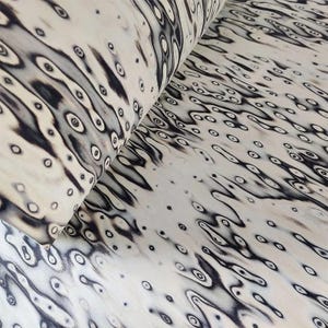 Pu&ograve; includere: Un rotolo di materiale color crema con un motivo ripetuto di forme organiche nere che ricordano occhi o gocce d'acqua. Il design crea un aspetto fluido e strutturato, adatto a vari progetti artigianali.