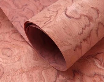 May include: A rolled sheet of reddish-brown wood veneer. The wood grain shows a swirling pattern. The veneer is curled, revealing the inner layers. The overall tone is warm and natural, suggesting a material for woodworking or crafts. The measurements are in centimeters.