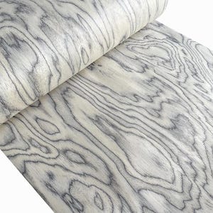 以下が含まれることがあります： 明るいグレーと白の色合いの木材ベニヤのロール。木目は、自然で流れるようなデザインを作り出す濃いグレーの線で目立ちます。ベニヤは丸められており、その層状の質感と詳細を示しています。