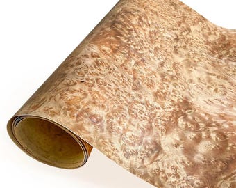 May include: A rolled sheet of wood veneer with a complex, swirling grain pattern. The veneer displays a warm, natural color palette of light and medium browns, with a textured, burl-like appearance. The edges of the roll reveal a contrasting, lighter-colored interior.