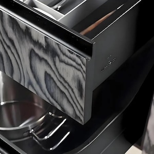 Puede incluir: Primer plano de un caj&oacute;n de cocina con frente de veta de madera. El caj&oacute;n est&aacute; abierto, revelando un soporte para utensilios de acero inoxidable y otros compartimentos. La veta de la madera tiene un patr&oacute;n gris y blanco. El caj&oacute;n es parte de un gabinete negro m&aacute;s grande.